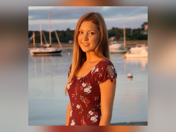 Mieke Oort is a white female with long, light brown hair. She is wearing a brown top with flowers as she stands in front of boats on the water.