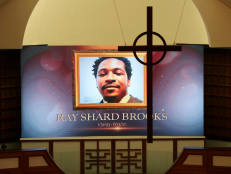 A cross hangs from the cathedral ceiling while Rayshard Brooks is memorialized on a screen during his public viewing in June 2020. [via AP Images/Curtis Compton/Atlanta Journal-Constitution]