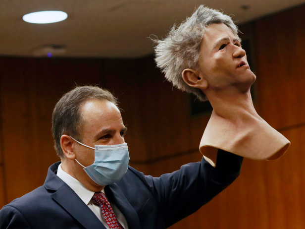 Attorney Habib A. Balian wearing a blue suit in court, holding a latex mask with gray hair that was worn by Robert Durst
