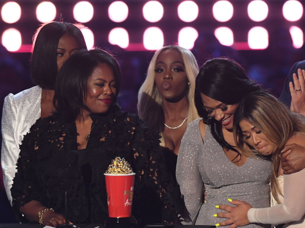 The photo is of a group of women in formal attire accepting an award from MTV for their film.