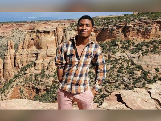 Daniel Robinson wears a plaid shirt and pink pants standing in front of the Grand Canyon