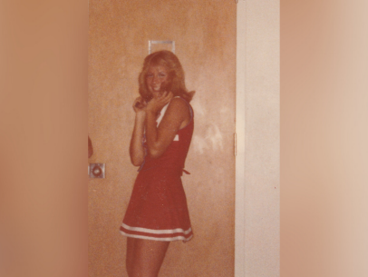Retha Stratton is a white female with blonde hair who was murdered in 1982. In this sepia toned photo, she's wearing a red cheerleading outfit and is standing in front of a brown wood door.