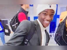 18-year-old Amara Jones smiles and wears a white beanie hat, a grey suit jacket and a backpack pictured walking down a high school hallway