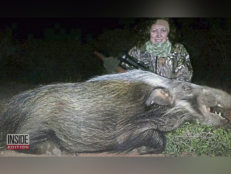 Bianca Finizio Rudolph sits smiling with a gun over a hog that she killed while hunting at night
