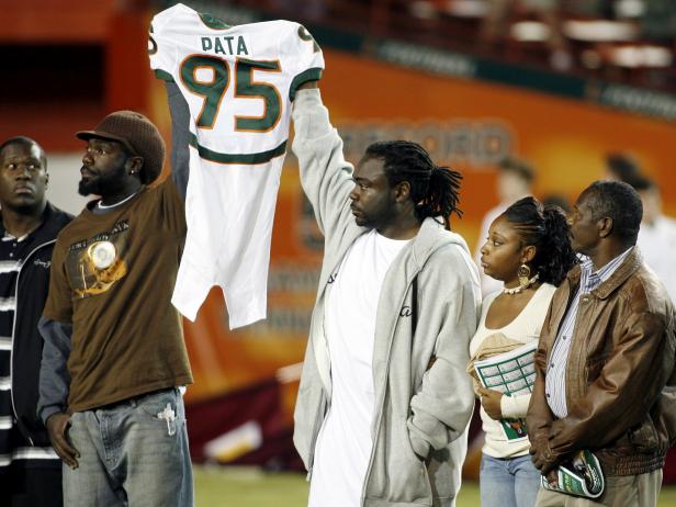 Two Black males, relatives of Bryan Pata, hold up his white number 95 University of Miami football jersey. Bryan Pata was fatally shot in 2006.