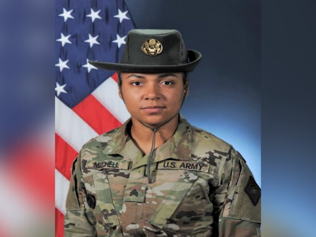 Staff Sergeant Jessica Ann Mitchell is a woman with brown skin. She is pictured with a black hat and Army fatigues.