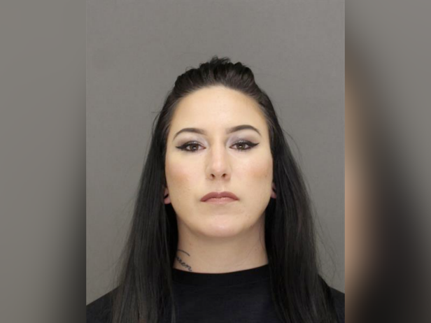 Taylor D. Schabusiness has dark brown hair and hazel eyes. In this mugshot, she's wearing heavy eyeliner and posed against a gray background.