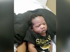 La'Mello Parker is a baby boy. He is shown with black curly hair wearing a black New Orleans Saints t-shirt.