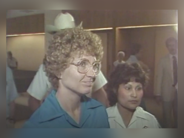 Candy Montgomery pictured leaving court after being on trial for killing Betty Gore. She is wearing glasses and a blue top. 