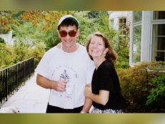 Michael Peterson [left] and Kathleen Peterson [right] smile. He is wearing sunglasses, a white shirt, and a hat and she is wearing a black shirt. 