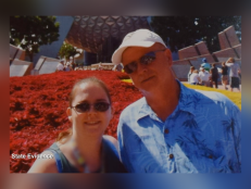 Molly Watson [left] and James Addie [right] pictured on vacation. They are both smiling and wearing sunglasses. He is wearing a white hat and a blue floral shirt. 