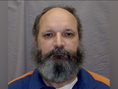 Prison photo of Donald Spice, who was charged with murdering his fiancée. Donald Spice wears a blue and orange jacket and has a grey beard. 