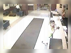 Surveillance photo of Megan Waterman at a hotel lobby front desk. She is wearing a yellow sweater.