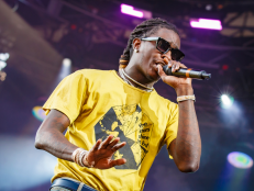 Young Thug performing at Osheaga Music and Art Festival in Montreal, Canada in August 2019. He is wearing black sunglasses and a yellow shirt. 