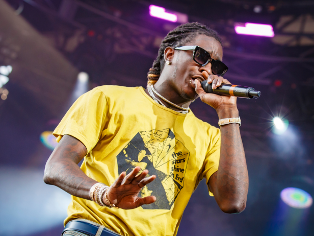 Young Thug performing at Osheaga Music and Art Festival in Montreal, Canada in August 2019. He is wearing black sunglasses and a yellow shirt. 