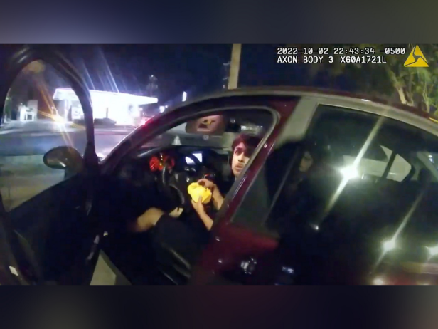 In this image taken from Sunday, Oct. 2, 2022, police body camera video and released by the San Antonio Police Department, Erik Cantu looks toward San Antonio Police Officer James Brennand while holding a hamburger in a fast food restaurant parking lot as the officer opens the car door in San Antonio, Texas. 